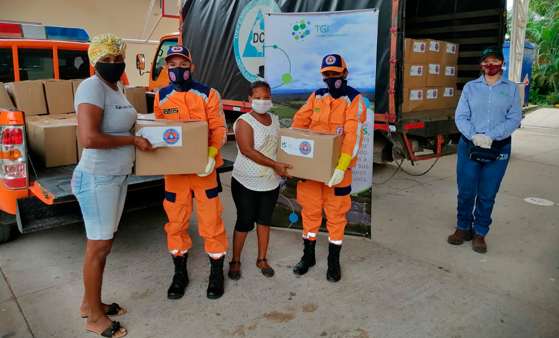 Dos hombres de la Defensa Civil le entregan dos cajas con ayudas humanitarias a dos mujeres de la comunidad