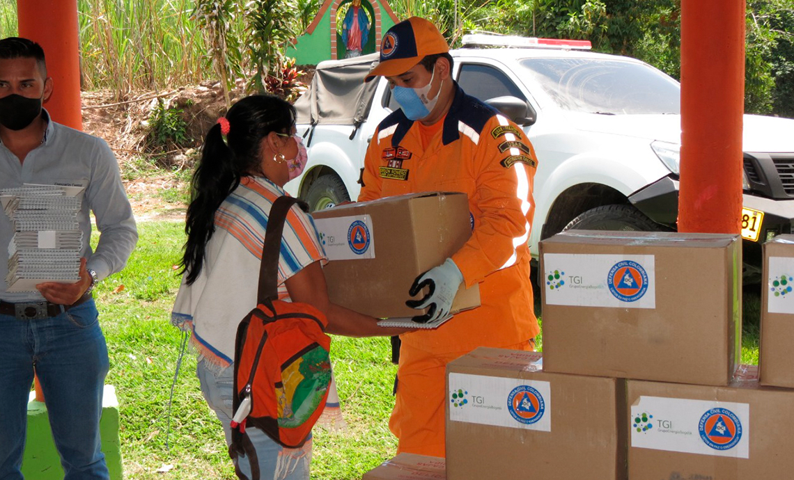 Un hombre de la Defensa Civil le entrega en sus manos a una mujer una caja con ayudas humanitarias
