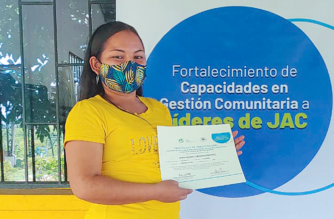 Una mujer sostiene sonriente su diploma como líder de una junta de acción comunal