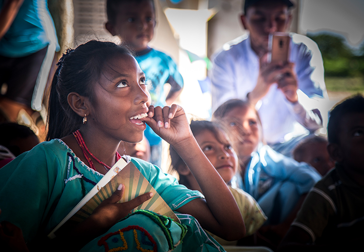 Niña de la comunidad wayú luce concentrada y sonríe con alegría acompañada de otros niños