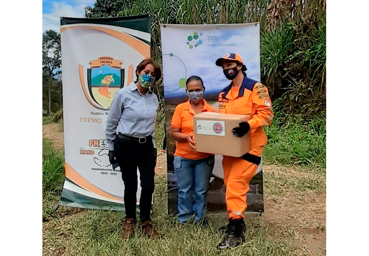 Una mujer de la Defensa Civil y una de TGI le entregan una caja a una señora de la comunidad