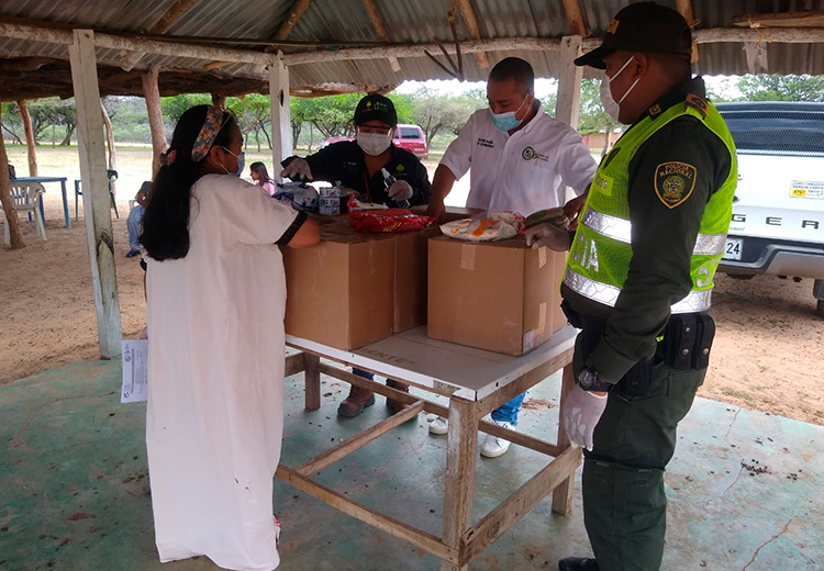 Dos personas coordinan la entrega de cajas con ayudas humanitarias, hay un policía al lado y una mujer de la comunidad wayú