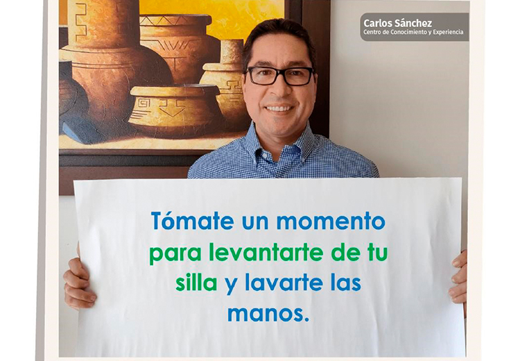 Carlos Sánchez con un letrero que dice: Tómate un momento para levantarte de tu silla y lavarte las manos