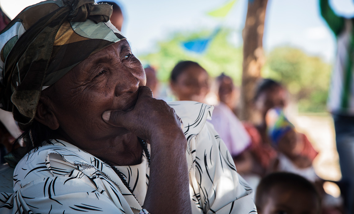 Señora mayor de la comunidad wayú mira a lo lejos concentrada con su mano cubriendo su boca